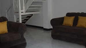 A living room with two dark brown sofas, each with a mustard yellow cushion, and a white spiral staircase in the background. - 256 Jamaica (Montego Bay)