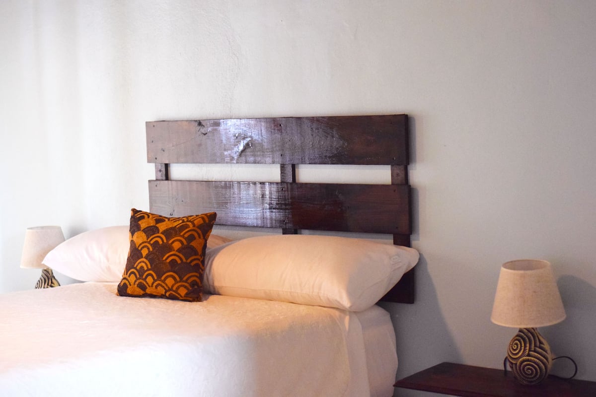Una cama con cabecera de madera, dos almohadas y una mesita de noche con lámpara.