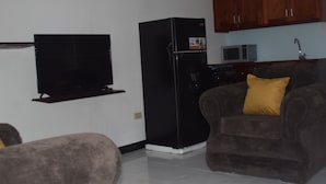 A living room with a flat-screen TV, a black refrigerator, a microwave, and a sofa with a yellow pillow. - 256 Jamaica (Montego Bay)