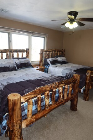Two beds with patterned bedspreads and matching pillows, a ceiling fan, and large windows.