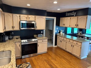 A kitchen with wooden cabinets, stainless steel appliances, granite countertops, and a 'family' sign on the wall. - Lux Cabin w/ hot tub, playground, game room, bb court,walking trail, resort pool (Hidden Valley)