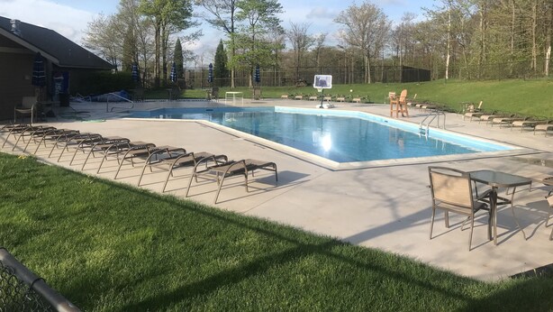 Una piscina con aro de baloncesto, sillas de descanso y una zona de estar techada.