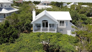 Une maison blanche à deux étages, dotée d’un balcon et entourée d’une végétation luxuriante.