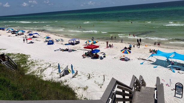 Une plage avec des parasols, des chaises longues et un escalier en bois qui descend vers le rivage.