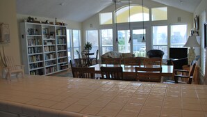 Un salon spacieux avec une grande bibliothèque, un coin repas comprenant une table et des chaises, et un ventilateur de plafond.