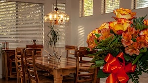 A dining area with a wooden table and chairs, a chandelier, and a vase of flowers with a red ribbon. - Resort Like Home W/Private Heated Swimming Pool / Power Ranch K1 Pickleball (Gilbert)
