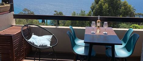 A balcony with a table and chairs, overlooking a scenic view of the sea.