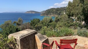 Two red metal chairs on a stone ledge overlooking a coastal landscape with greenery and distant hills. - Furnished 3 STARS Golf St Tropez RAYOL CANADEL Facing the SEA with POOL (Rayol-Canadel-sur-Mer)