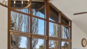 Un coin repas comprenant une table ronde en verre, quatre chaises rembourrées et de grandes fenêtres donnant sur un paysage arboré et un champ verdoyant.