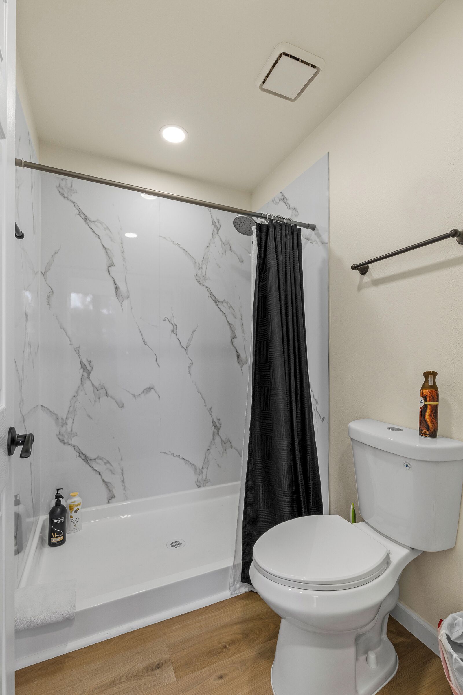 A bathroom with a white toilet, a shower with a black curtain, and a marble wall.