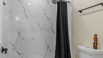 A bathroom with a white toilet, a shower with a black curtain, and a marble wall.