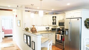 A modern kitchen with white cabinets, stainless steel appliances, and a central island with bar stools. - Beautifully Renovated Downtown Luxury Condo, a block from the rock!   (Plymouth)