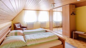 A room with a sloped ceiling, wooden walls, a bed with striped bedding, a chair, and a wardrobe.