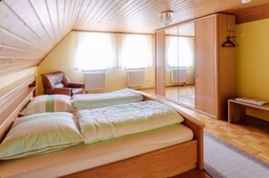 A room with a sloped ceiling, wooden walls, a bed with striped bedding, a chair, and a wardrobe.