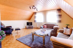 Ein gemütliches Wohnzimmer mit Holzbalkendecke, einer Couch, einem Couchtisch und einem Fernseher.
