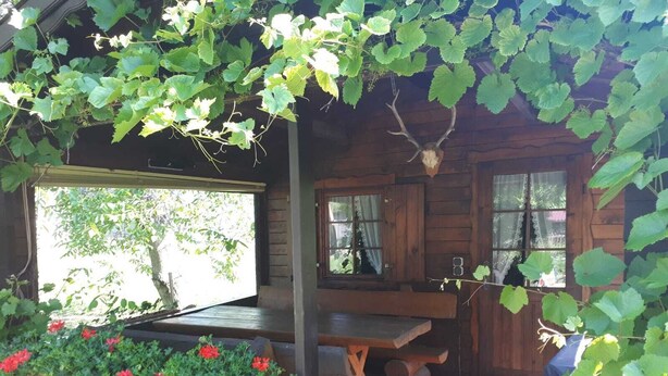 A rustic wooden cabin with a covered porch, a dining table, and a bench.