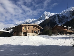 Een houten chalet met een met sneeuw bedekte dak, tegen een achtergrond van besneeuwde bergtoppen en een heldere lucht.