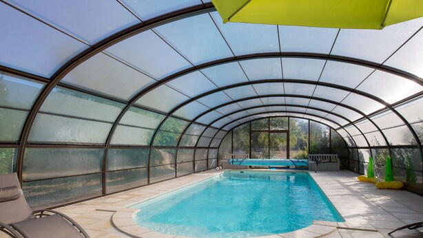 An indoor swimming pool with a glass ceiling, a lounge chair, and a yellow umbrella.