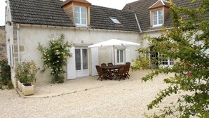 A two-story house with a gravel driveway, a patio with a table and chairs, and a white umbrella.