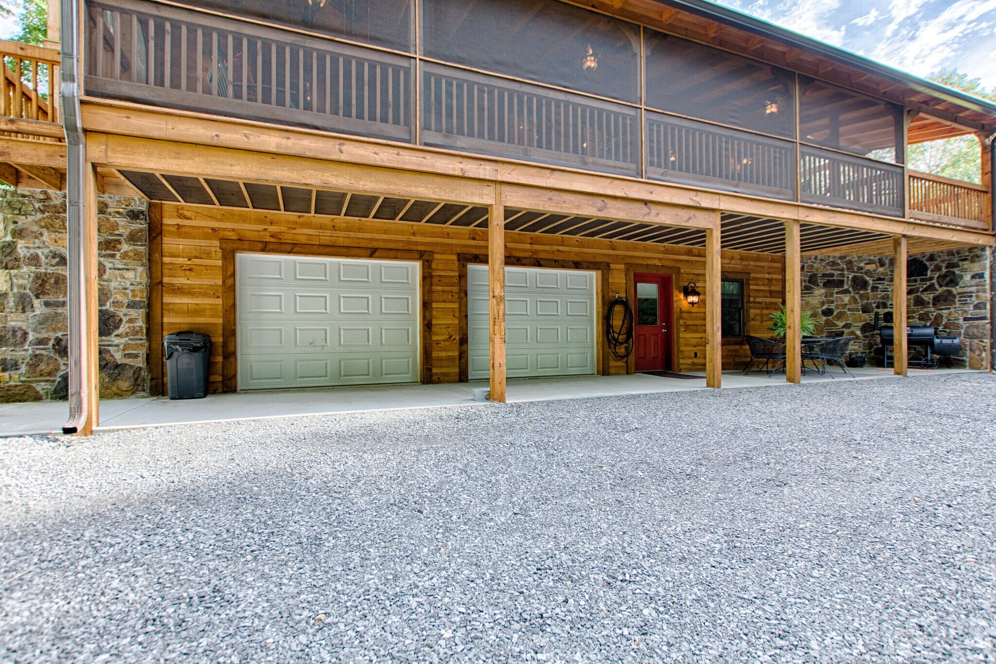 A two-story log cabin with a covered porch, stone walls, and two garage doors.