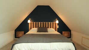 Une chambre avec un plafond en pente, un lit doté d’une tête de lit grise, deux lampes de chevet et un mur de couleur sombre.