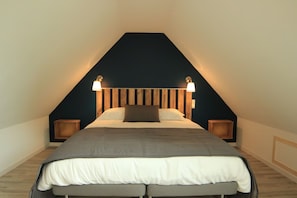 A bedroom with a sloped ceiling, a bed with a grey headboard, two bedside lamps, and a dark wall.