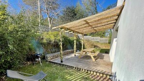 Un jardin avec une terrasse en bois, une pergola et un barbecue.