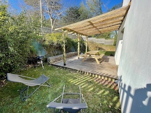 A backyard with a wooden deck, a pergola, and a barbecue grill.