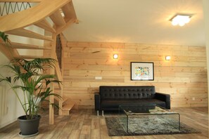 Une pièce avec un escalier en bois, un canapé en cuir noir, une table basse en verre et une plante en pot.