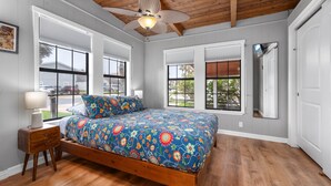 Ein Schlafzimmer mit einem hölzernen Bett, einem Deckenventilator und großen Fenstern.