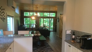 A modern kitchen with granite countertops, wooden flooring, and large windows offering a view of the outdoors.