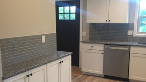 A kitchen with white cabinets, a black door, and a window.