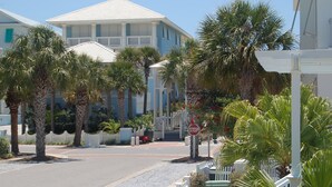 A street view with a white building with balconies, palm trees, and a stop sign. - "The Odyssea" - Carillon Beach - Beautiful Home Two Lots From Beach!  (Panama City Beach)