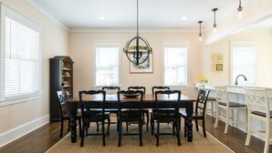 A dining room with a wooden table and chairs, a chandelier, and a kitchen area with a sink and counter. - "The Odyssea" - Carillon Beach - Beautiful Home Two Lots From Beach!  (Panama City Beach)