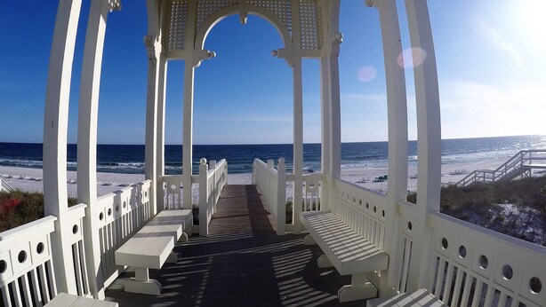 A covered outdoor area with white columns and benches, overlooking a beach. - "The Odyssea" - Carillon Beach - Beautiful Home Two Lots From Beach!  (Panama City Beach)