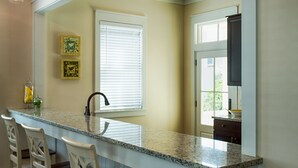 A kitchen with a marble countertop, white bar stools, pendant lighting, and a window with blinds. - "The Odyssea" - Carillon Beach - Beautiful Home Two Lots From Beach!  (Panama City Beach)