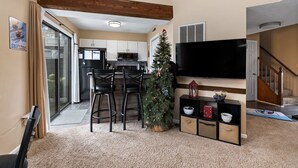 A modern living room with a large flat-screen TV, a small Christmas tree, and a staircase leading to another level.