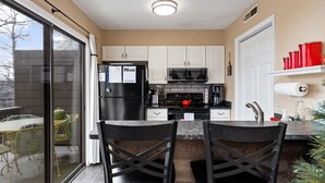 A compact kitchen with white cabinets, a black refrigerator, a microwave, and a stove. There are two black chairs and a small dining table.