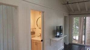 A hallway with a bathroom, a mounted TV, and a view of trees through a window.