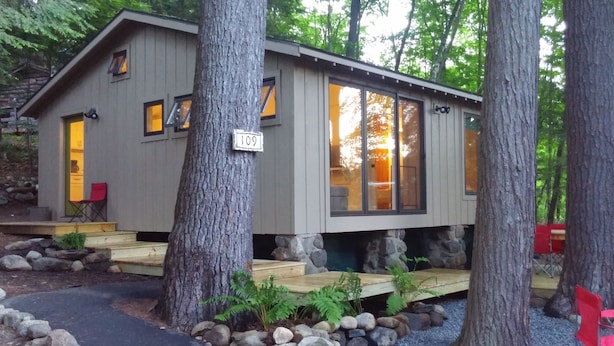 A cabin with a stone foundation, large windows, and a wooden deck.