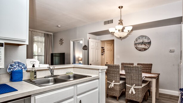 A modern kitchen with a built-in dishwasher, a sink, and a dining area with wicker chairs and a wooden table. - Charming, newly reno 1Bdrm condo, minutes from beautiful Clearwater Beach (Clearwater)