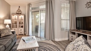 A modern living room with a sofa, coffee table, TV stand, and a glass door leading to a balcony. - Charming, newly reno 1Bdrm condo, minutes from beautiful Clearwater Beach (Clearwater)