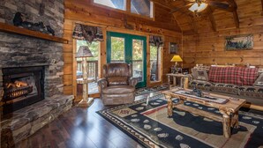 A log cabin interior with a stone fireplace, leather armchair, wooden coffee table, and a plaid sofa. - Cozy, View, NFL Sunday, SuperFast WiFi, Arcade, Gated, Fishing & 2 Pools, Gated! (Sevierville,)