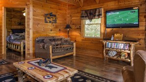 A cozy log cabin interior with a wooden floor, a sofa, a coffee table, a television, and a bookshelf. - Cozy, View, NFL Sunday, SuperFast WiFi, Arcade, Gated, Fishing & 2 Pools, Gated! (Sevierville,)