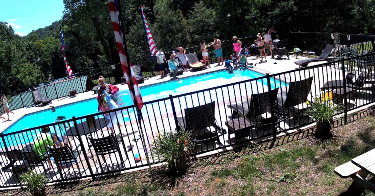 Ein Schwimmbecken mit einem umzäunten Deckbereich, umgeben von Stühlen und Blumentöpfen.
