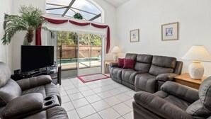 A living room with a sofa, a television, a lamp, and a large window with curtains. - 4BR Disney Oasis: Private Screened Pool + FREE Pool Heat! (20 Min to Parks) (Kissimmee)