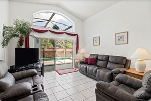 A living room with a sofa, a television, a lamp, and a large window with curtains.