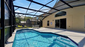 A swimming pool with a glass enclosure, a patio area with chairs, and a view of the surrounding neighborhood. - 4BR Disney Oasis: Private Screened Pool + FREE Pool Heat! (20 Min to Parks) (Kissimmee)