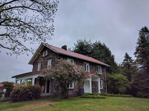 A two-story stone house with a red roof, a porch, and a garden. - Stonehouse w/ Hot Tub, Walk to GAP Trail & Town (Confluence)