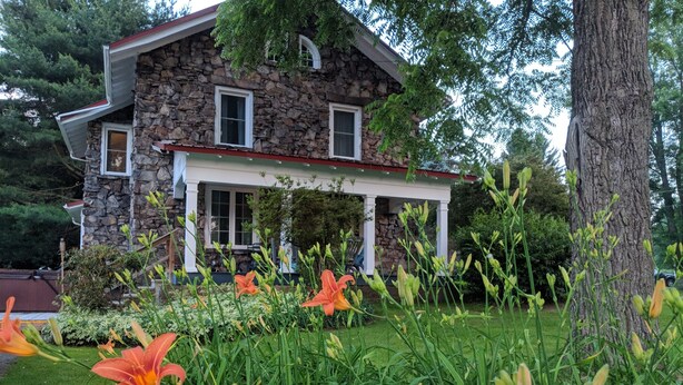 A stone house with a covered porch and a garden with orange flowers. - Stonehouse w/ Hot Tub, Walk to GAP Trail & Town (Confluence)